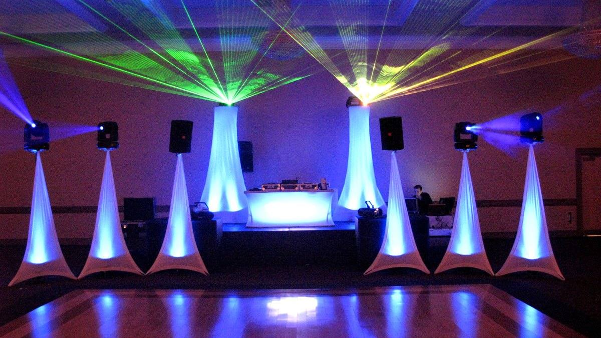 A Toronto ballroom rigged for a reception: white drape cones uplit blue and violet, the booth centred, the dance floor still empty and beams across the ceiling