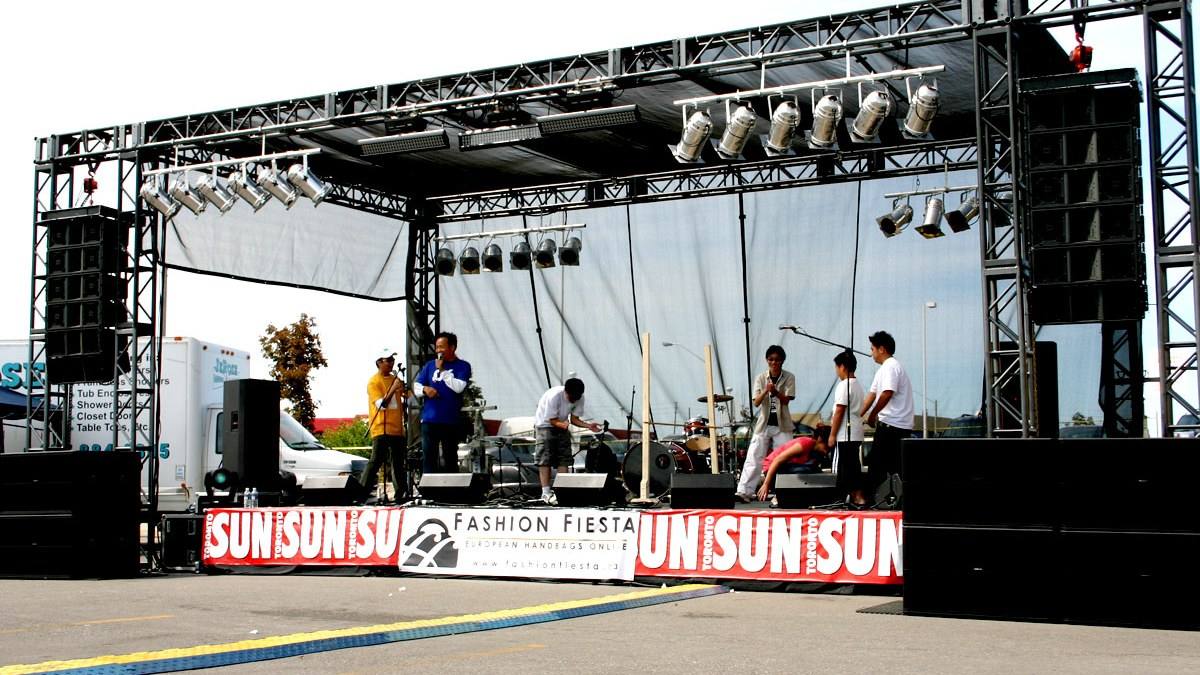 Outdoor stage with a band playing to a street crowd in daylight
