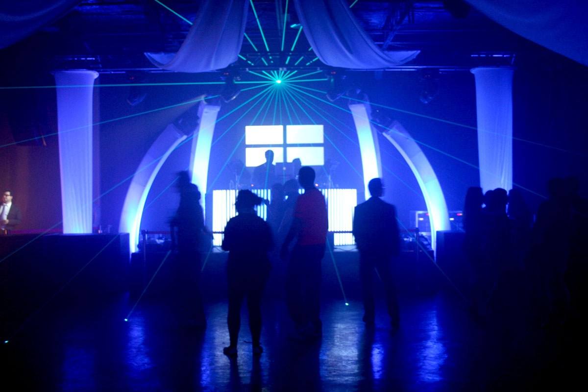 Dance floor filling under arched white drape uplit blue, guests dancing in silhouette at a club night