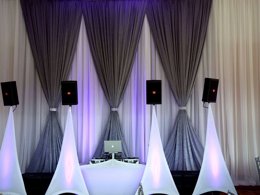 White pipe and drape run behind a stage position, speakers either side, washed from below in blue and violet
