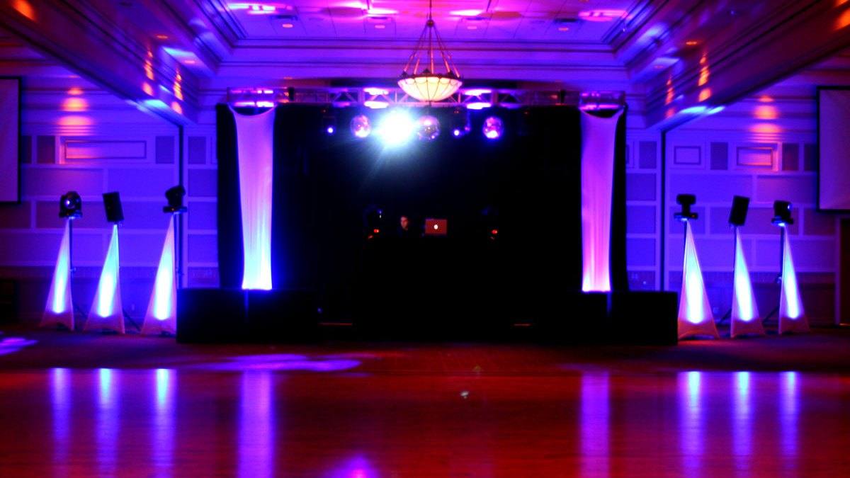 Banquet hall under magenta and violet uplighting, chandelier lit, tables set and the floor still empty before doors